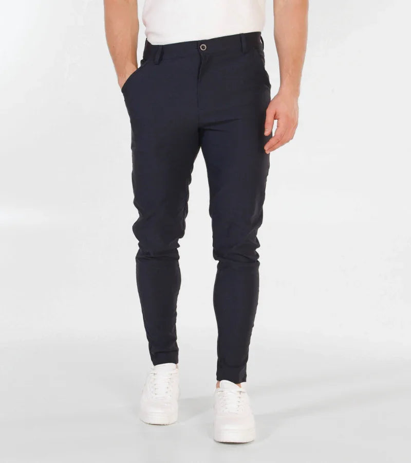 man wearing slim-fit navy blue trousers with white sneakers and white shirt