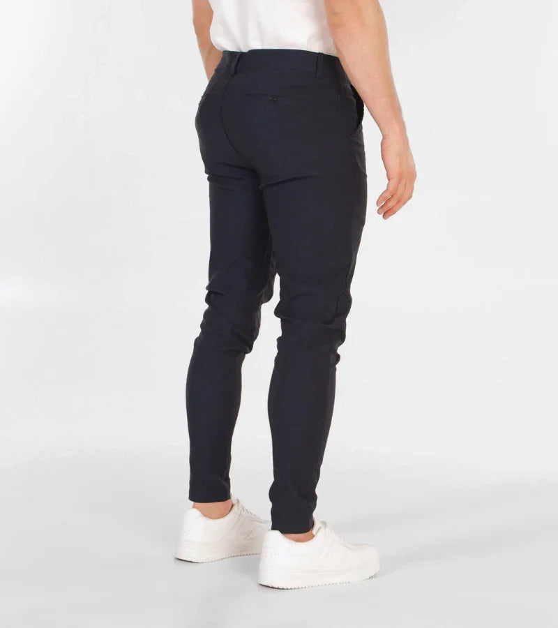 Back view of man wearing slim fit navy blue pants with white sneakers on white background