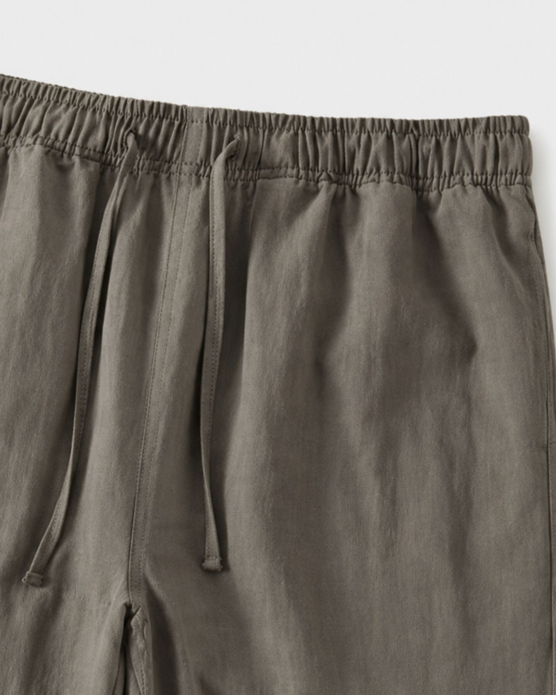 By Alden olive green linen drawstring trousers, close-up detail of elastic waistband and drawstring, light gray background #color_olive green