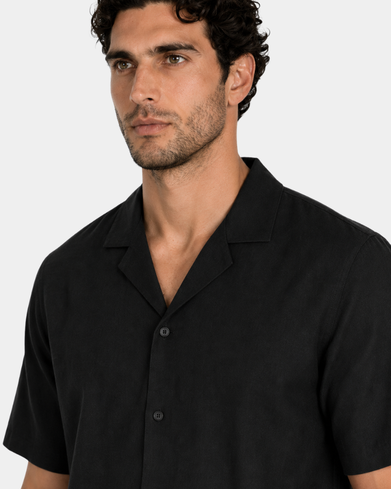 By Alden Black Linen Camp Collar Shirt worn by a male model, close-up front angle view of collar and button detail, light grey background #Color_black