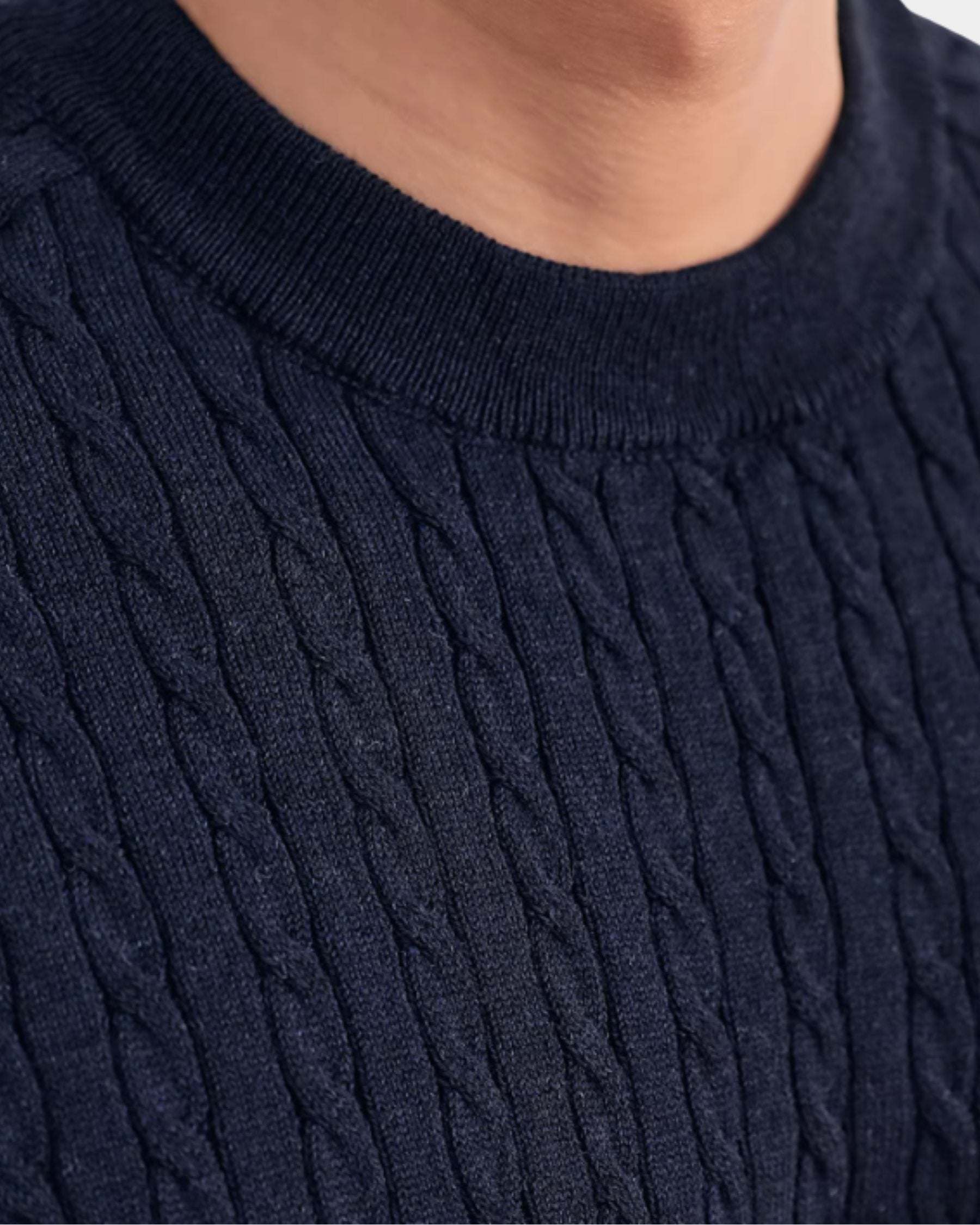 By Alden navy cable-knit short-sleeve sweater, close-up detail of crew neck and knit texture, outdoor background #color_navy