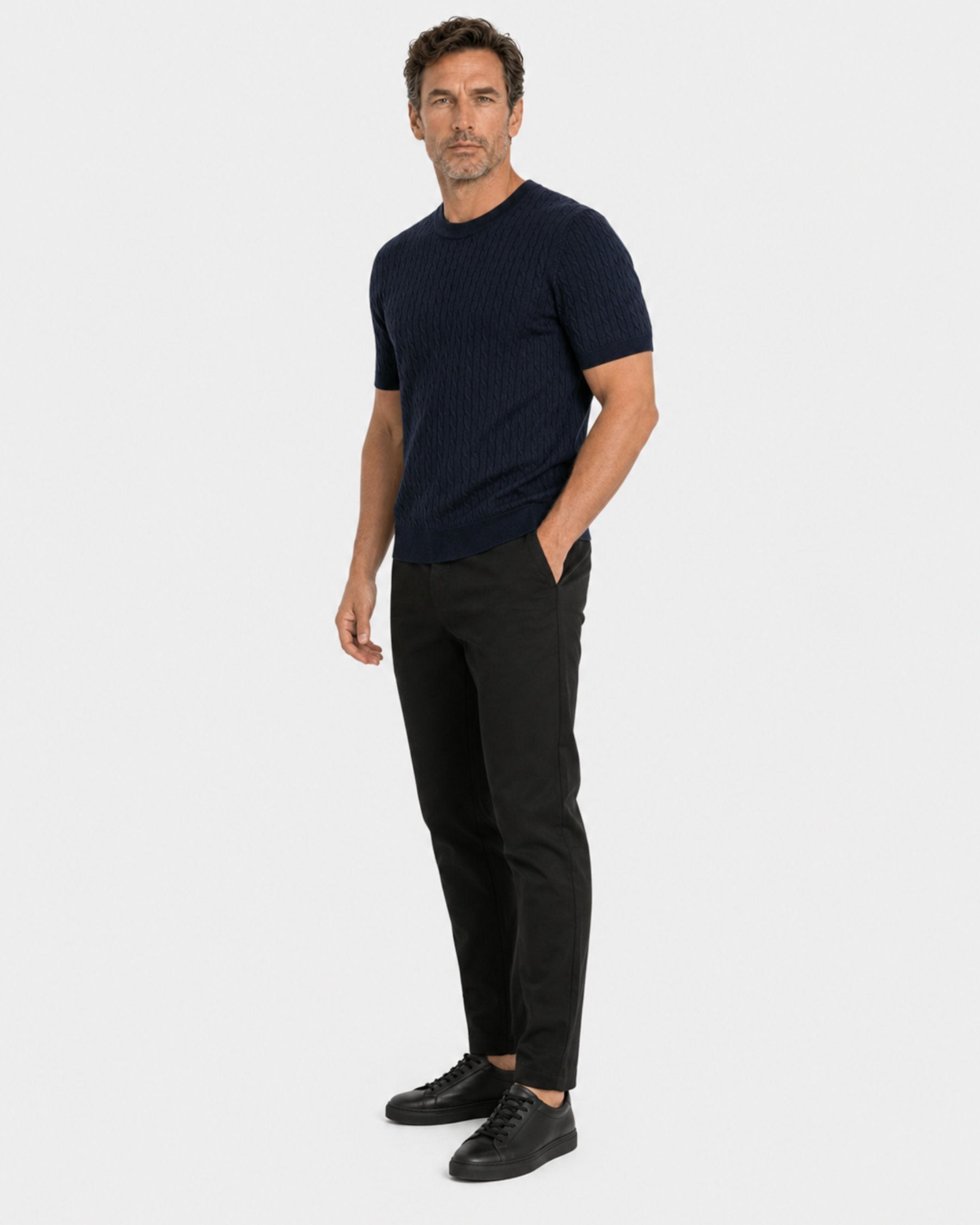 By Alden navy cable-knit short-sleeve sweater on male model, three-quarter view full body, light gray background #color_navy