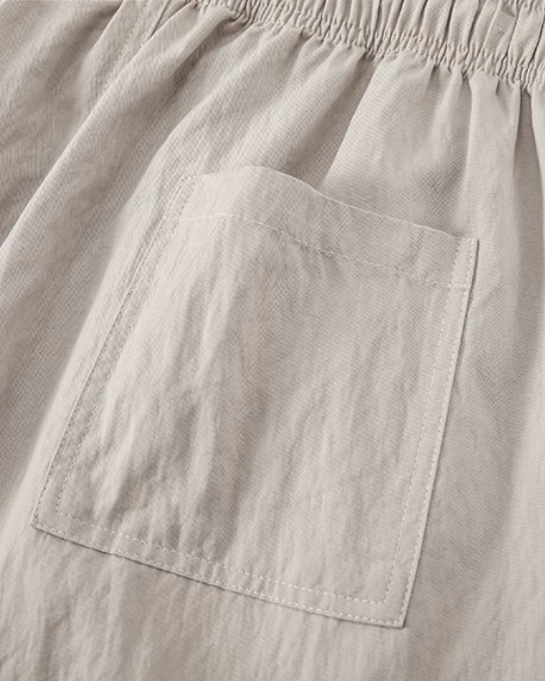 By Alden stone linen drawstring trousers, close-up detail of back pocket and fabric texture, light gray background #color_stone