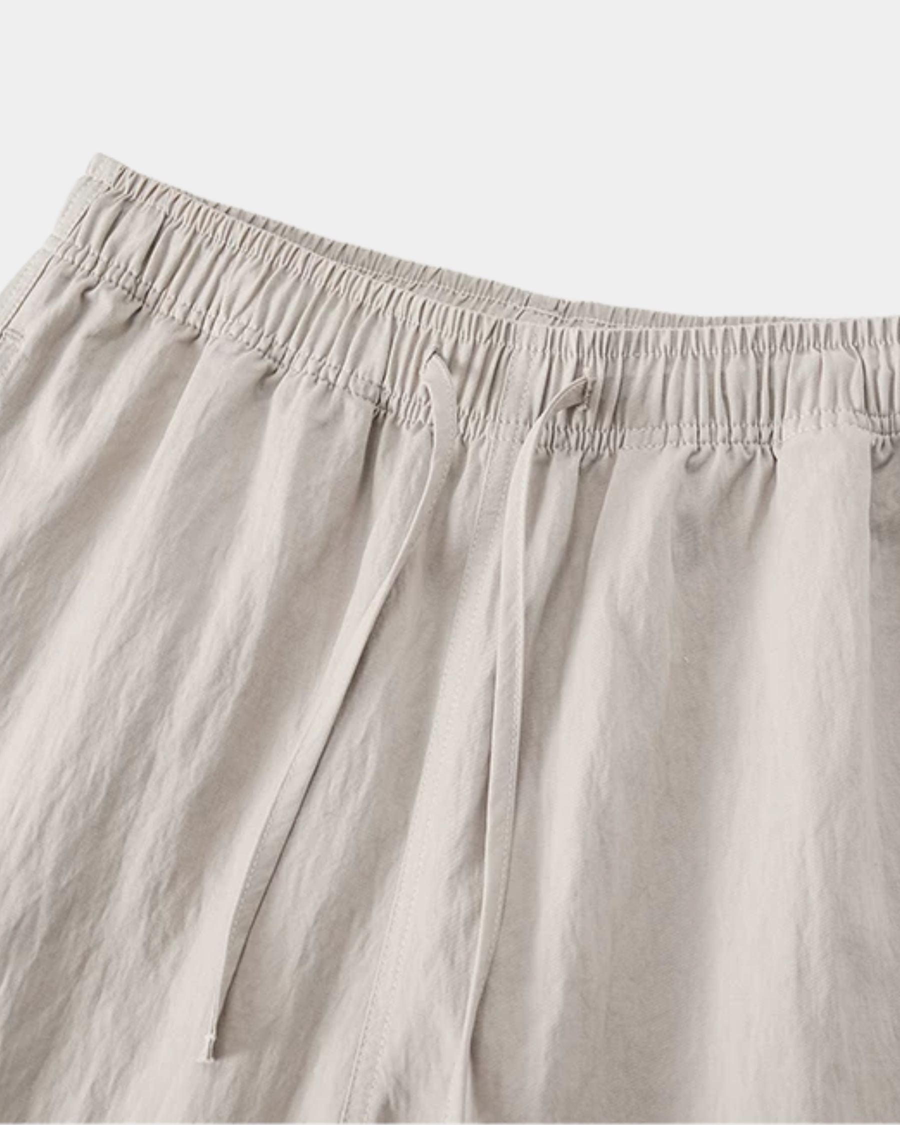 By Alden stone linen drawstring trousers, close-up detail of elastic waistband and drawstring, light gray background #color_stone