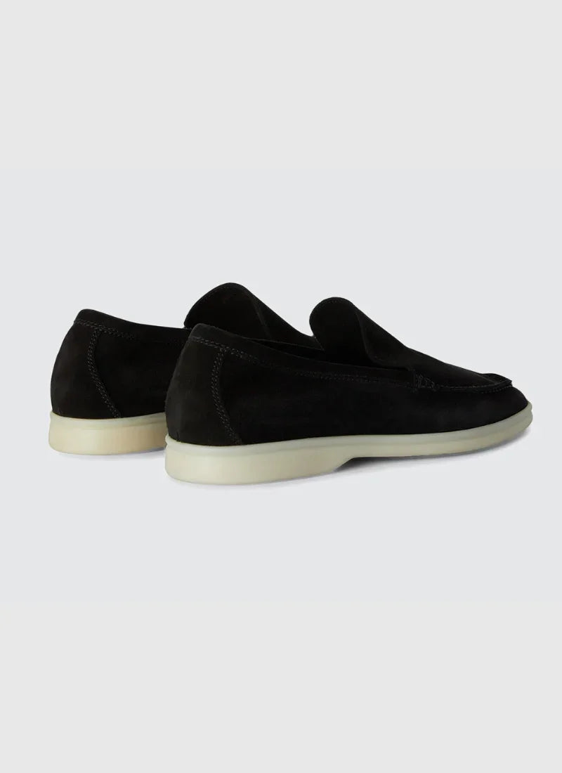 Pair of black suede yacht loafers with white soles on light gray background