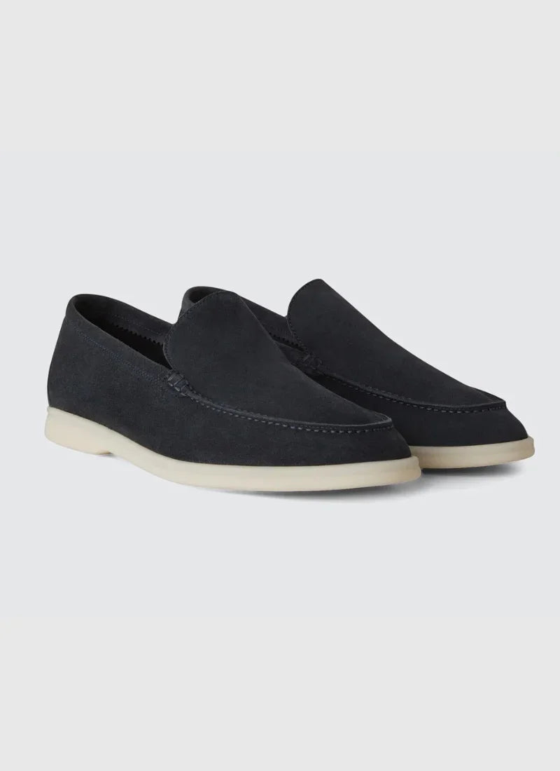 Pair of black suede yacht loafers with white rubber soles on gray background