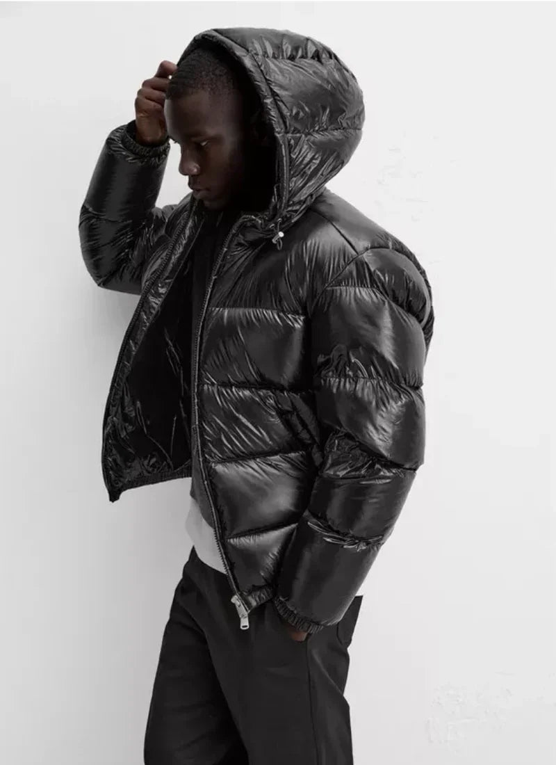 Black shiny puffer jacket with hood worn by a man against white background