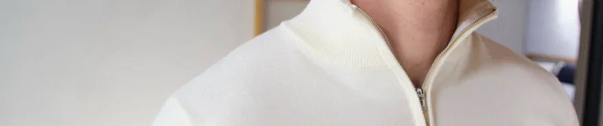 Close-up of a person wearing a cream-colored zip-up sweater with a ribbed collar and silver zipper