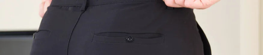 Close-up of a person wearing black pants with a buttoned back pocket in an indoor setting