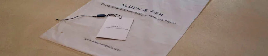 A white Alden & Ash branded dust bag with a product tag on a beige surface, showcasing craftsmanship packaging