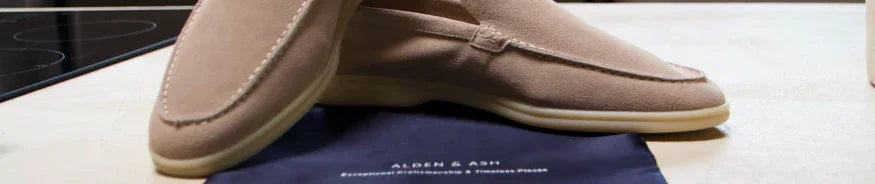 tan suede loafers placed on a dark blue Alden & Ash branded cloth on wooden surface