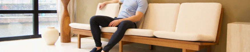 Man sitting on modern beige sofa in minimalist living room with large window and wooden decor