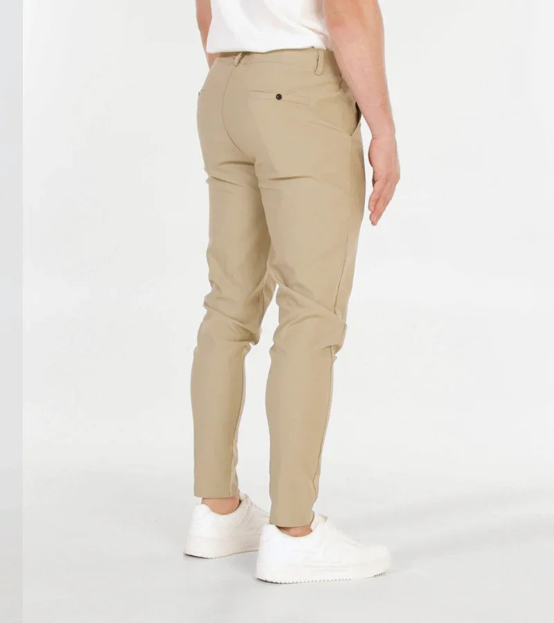 Rear view of man wearing slim beige pants and white sneakers against white background