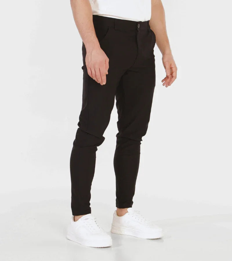 Man wearing slim fit black pants and white sneakers on white background
