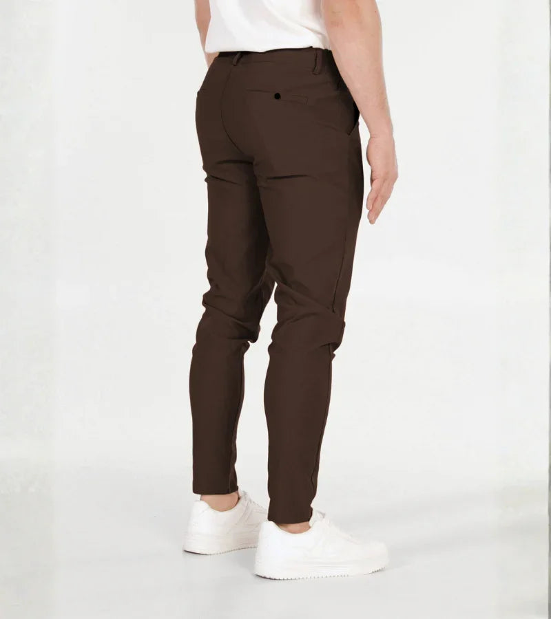 Man wearing slim-fit dark brown pants and white sneakers against a white background