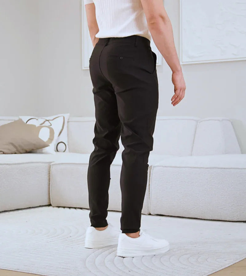 Man wearing black slim-fit pants and white sneakers standing in a modern living room