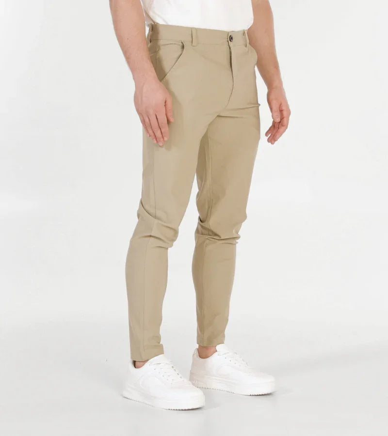 Man wearing slim-fit beige chinos and white sneakers against a white background