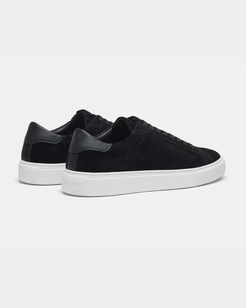 Luxury black suede trainers showcasing the smooth leather heel tab and clean white rubber sole from the back.