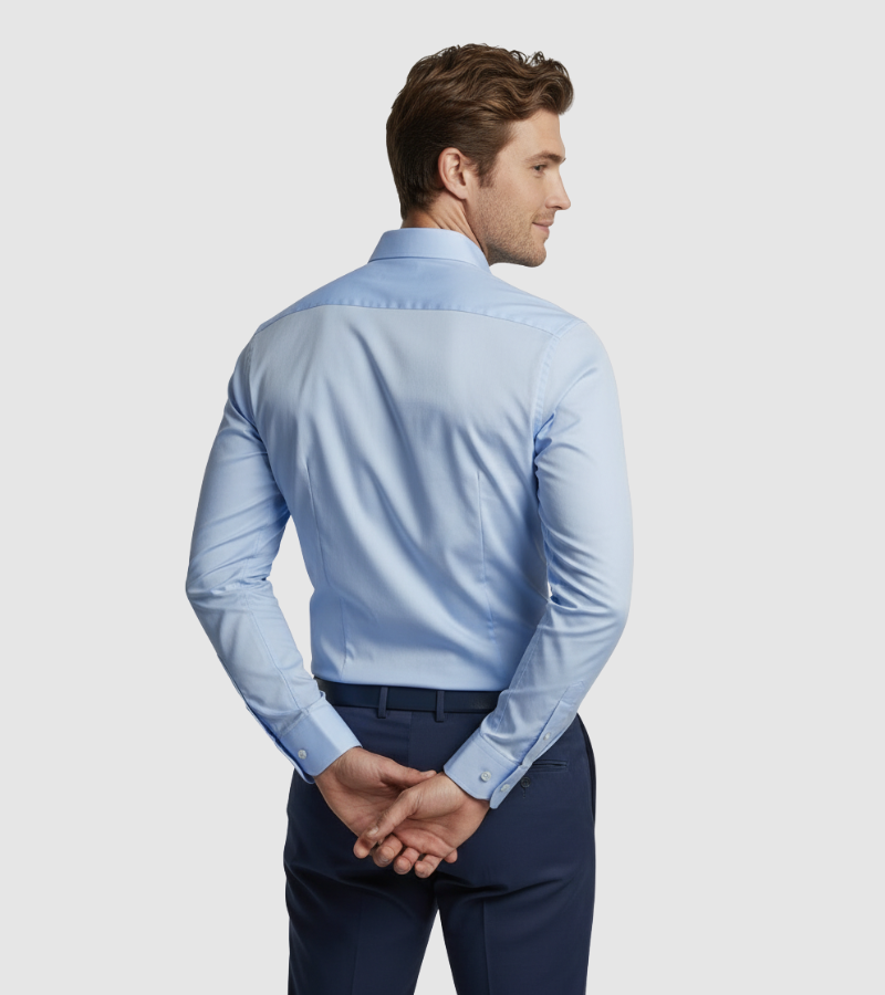 Man wearing a light blue dress shirt and dark blue pants on a plain background