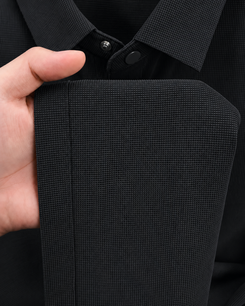 By Alden black knit polo shirt fabric texture detail, male model holding hem, extreme close-up, black background. #color_black