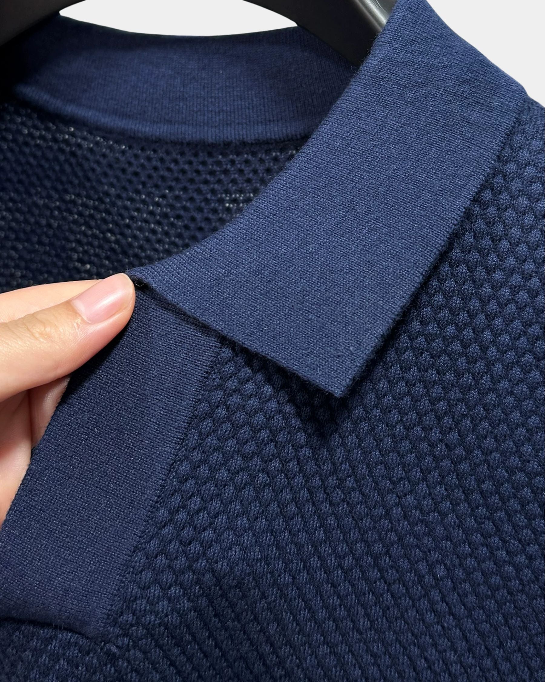 By Alden navy open-collar knit polo shirt collar and fabric texture detail, hand holding collar, close-up, navy background. #Color_navy
