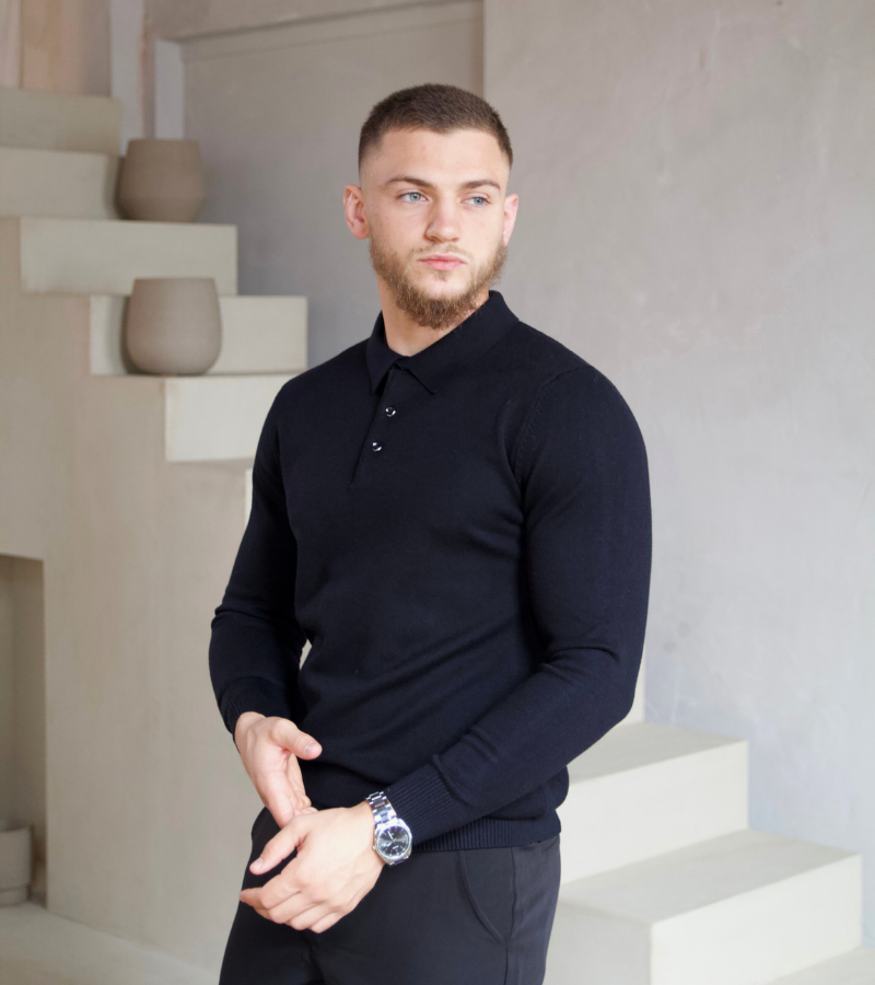 Man wearing a dark blue sweater standing in a modern indoor setting.